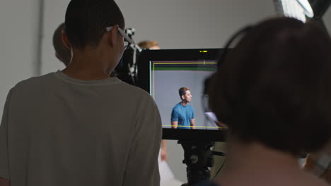 Actors-With-Scripts-In-Rehearsal-Shooting-Movie-Or-Video-In-Studio-With-Film-Crew-And-Female-Director-Watching-Monitor-In-Background